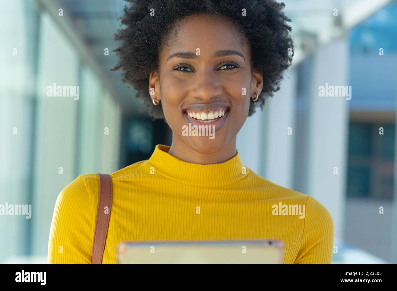Porträt einer lächelnden jungen afroamerikanischen Geschäftsfrau mit Afro-Frisur, die einen Tablet-pc hält Stockfoto