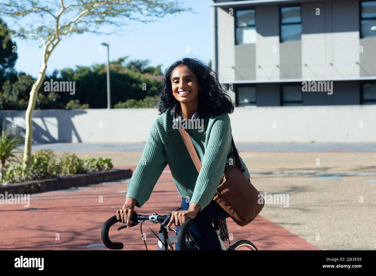 Porträt einer glücklichen jungen Biracial-Frau, die Fahrrad fährt, während sie am sonnigen Tag in der Stadt pendelt Stockfoto
