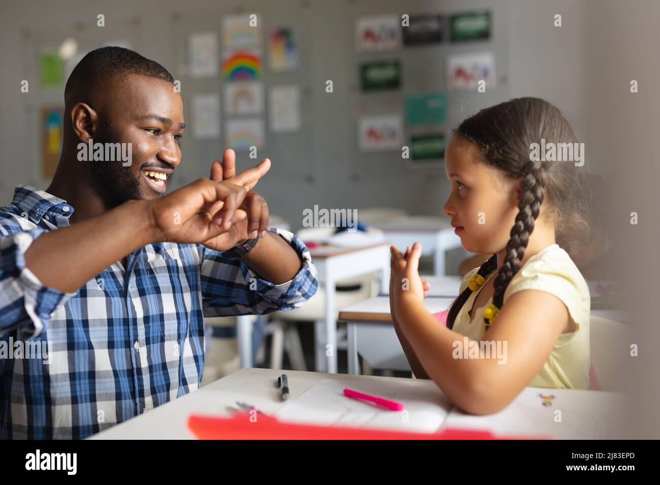 Lächelnder afroamerikanischer junger männlicher Lehrer, der dem kaukasischen Elementarmädchen Zeichensprache beibringt Stockfoto