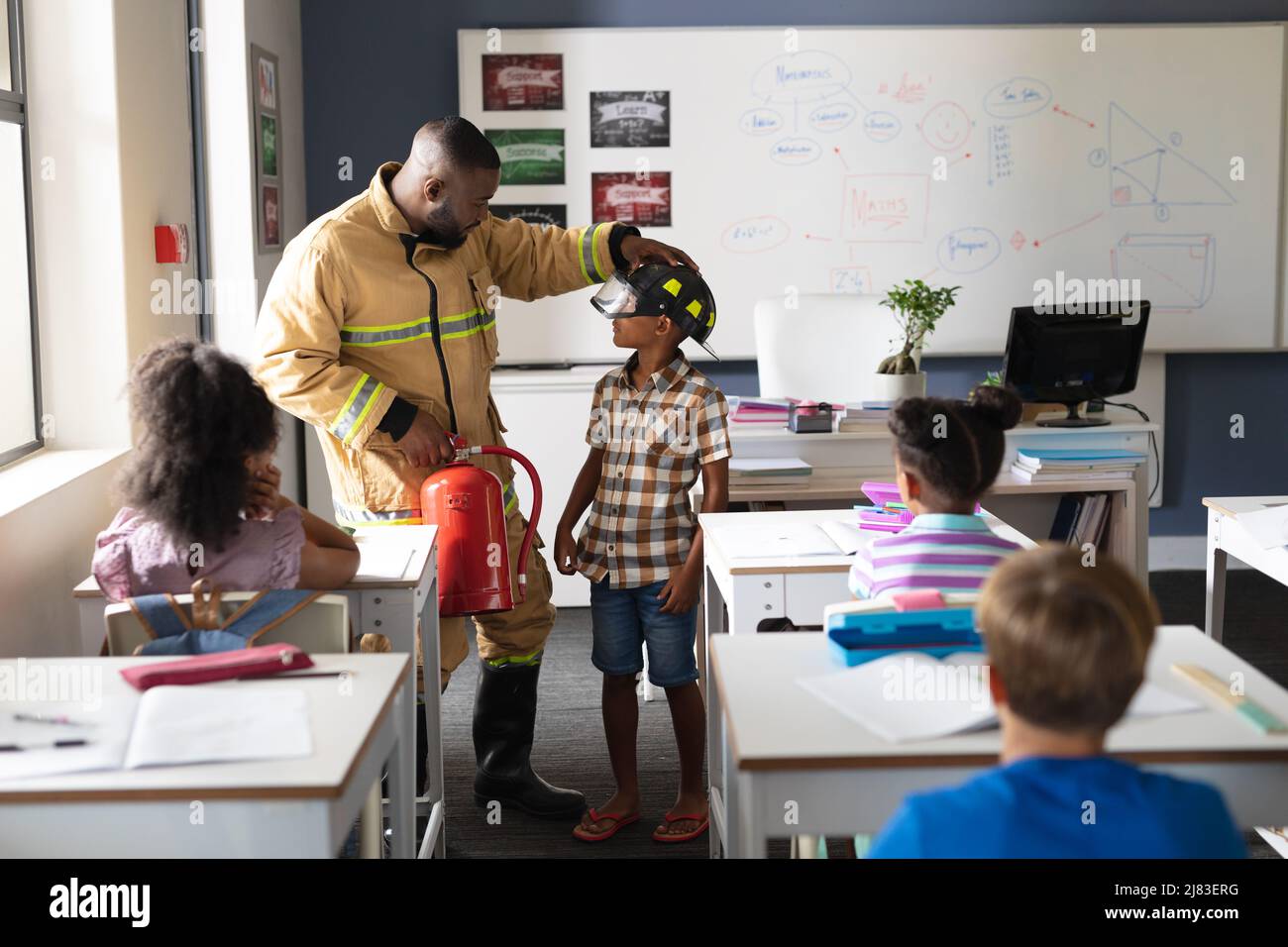 afroamerikanischer junger Lehrer mit Schutzhelm für afroamerikanischen Jungen in der Klasse Stockfoto