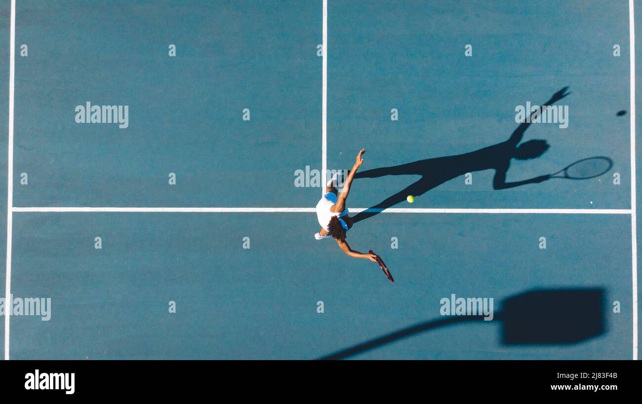 Blick von oben auf die junge afroamerikanische Spielerin, die an sonnigen Tagen auf dem blauen Tennisplatz Dienst Stockfoto