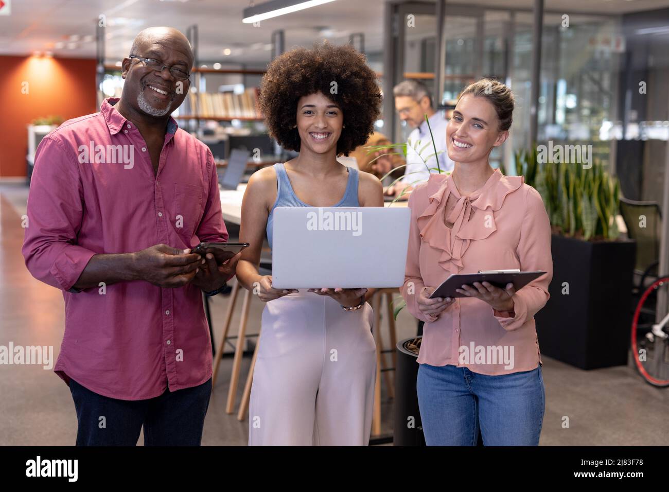 Porträt lächelnder, multirassischer Kollegen, die mit drahtlosen Technologien am modernen Arbeitsplatz stehen Stockfoto