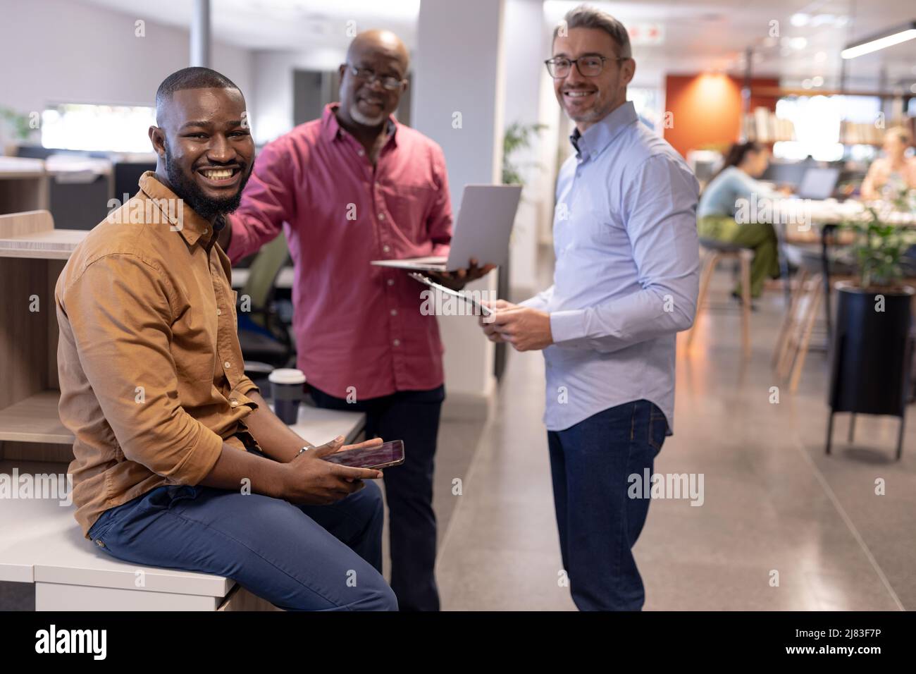 Porträt lächelnder, multirassischer männlicher Geschäftskollegen mit drahtlosen Technologien im modernen Büro Stockfoto