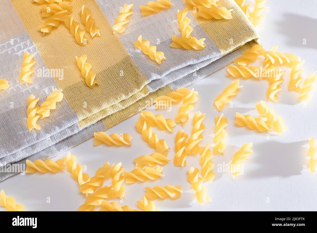 Ungekochte Fusilli Pasta auf weißem Tisch verstreut. Rohe und trockene Macaroni. Fett und ungesunde Lebensmittel Stockfoto