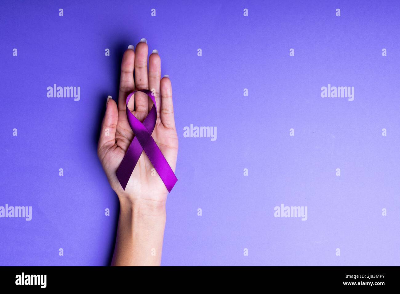 Beschnittene Hand einer afroamerikanischen Frau mit mittlerem Erwachsenen, die ein violettes Bewusstseinsband auf blauem Hintergrund hält Stockfoto