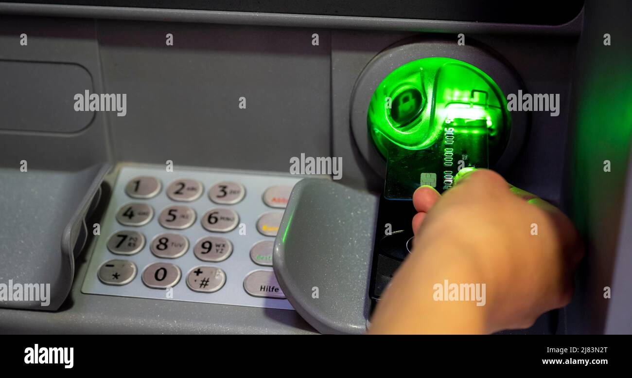 Hand schiebt Kreditkarte in einen Geldautomaten, gibt Geheimcode ein, zieht Geld ab Stockfoto