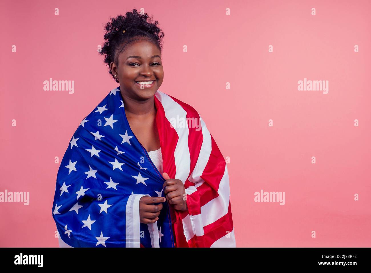 Lächelnde afroamerikanische Frau mit US-Flagge und Blick auf die Kamera im Studio rosa Hintergrund Stockfoto