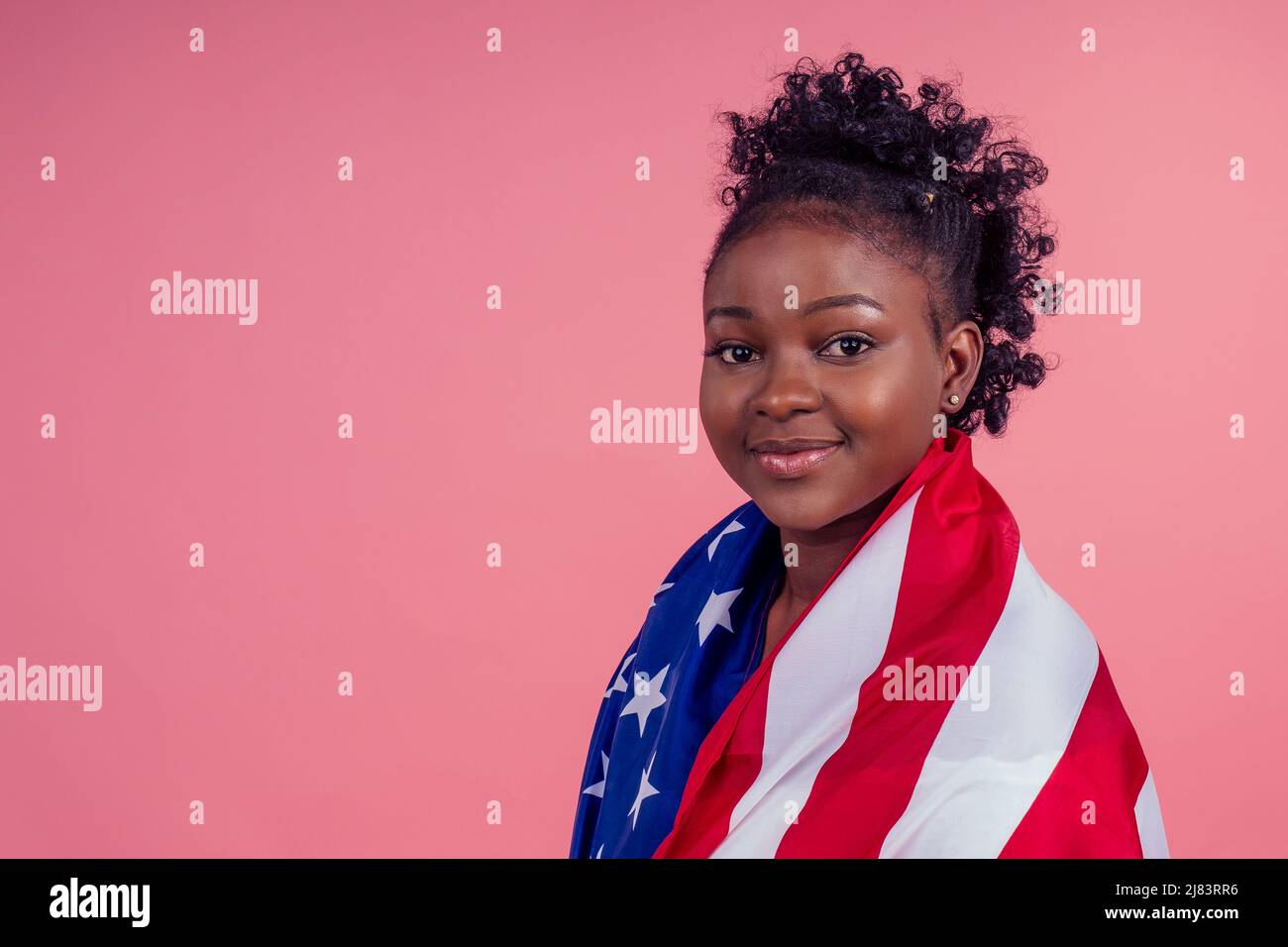 Lächelnde afroamerikanische Frau mit US-Flagge und Blick auf die Kamera im Studio rosa Hintergrund Stockfoto