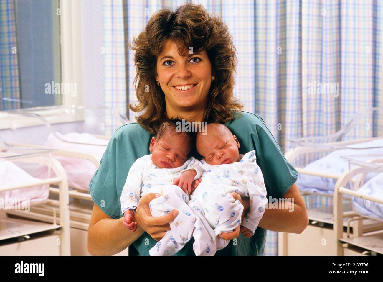 1980S LÄCHELNDE MUTTERSCHAFTSSCHWESTER, DIE AUF DIE KAMERA SCHAUT UND NEUGEBORENE AFROAMERIKANISCHE ZWILLINGSJUNGEN IM KRANKENHAUS HÄLT - KM9424 NET002 HARS NOSTALGIE-KRANKENSCHWESTERN ALTE MODE 1 JUVENILE WILLKOMMEN GLEICHGEWICHT STILLENDE SÄUGLING ZWILLING IDENTISCH DOPPELT ERFREUT FREUDE LIFESTYLE FRAUEN GESUNDHEIT HEIM LEBEN KOPIEREN RAUM DAMEN PERSONEN INSPIRATION SPIEL FÜRSORGLICH MÄNNER AUGENKONTAKT GESUNDHEITSVERSORGUNG PASSEND GLEICHEN ERFOLG BERUF GLÜCK ANBIETER FRÖHLICH ANBIETER ÄRZTE HEILUNG AFRO-AMERIKANER AFROAMERIKANISCHE SCHWARZE ETHNIE MUTTERSCHAFT STOLZ GESUNDHEIT PFLEGE BERUFE GESCHWISTER LÄCHELT HEILER FRÖHLICHE PRAKTIZIERENDE BABY JUNGE LOOK-ALIKE Stockfoto