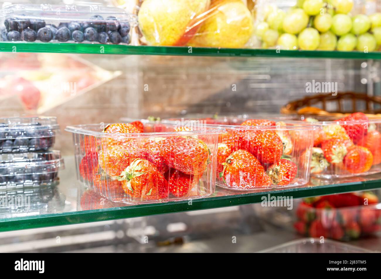 Frische reife Erdbeeren und andere Früchte auf einem Glasregal in einem Laden Stockfoto