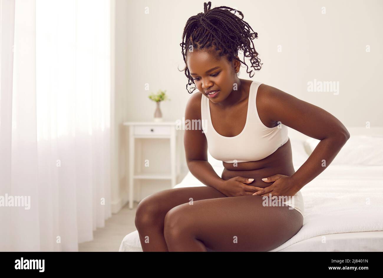 Schwarze Frau, die unter Bauchschmerzen leidet, sitzt auf dem Bett und berührt ihre linke Seite Stockfoto