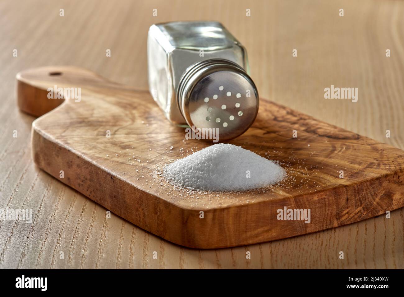 Verschüttetes Salz und ein Salzstreuer auf einem Schneidebrett aus Olivenholz - Nahaufnahme Stockfoto