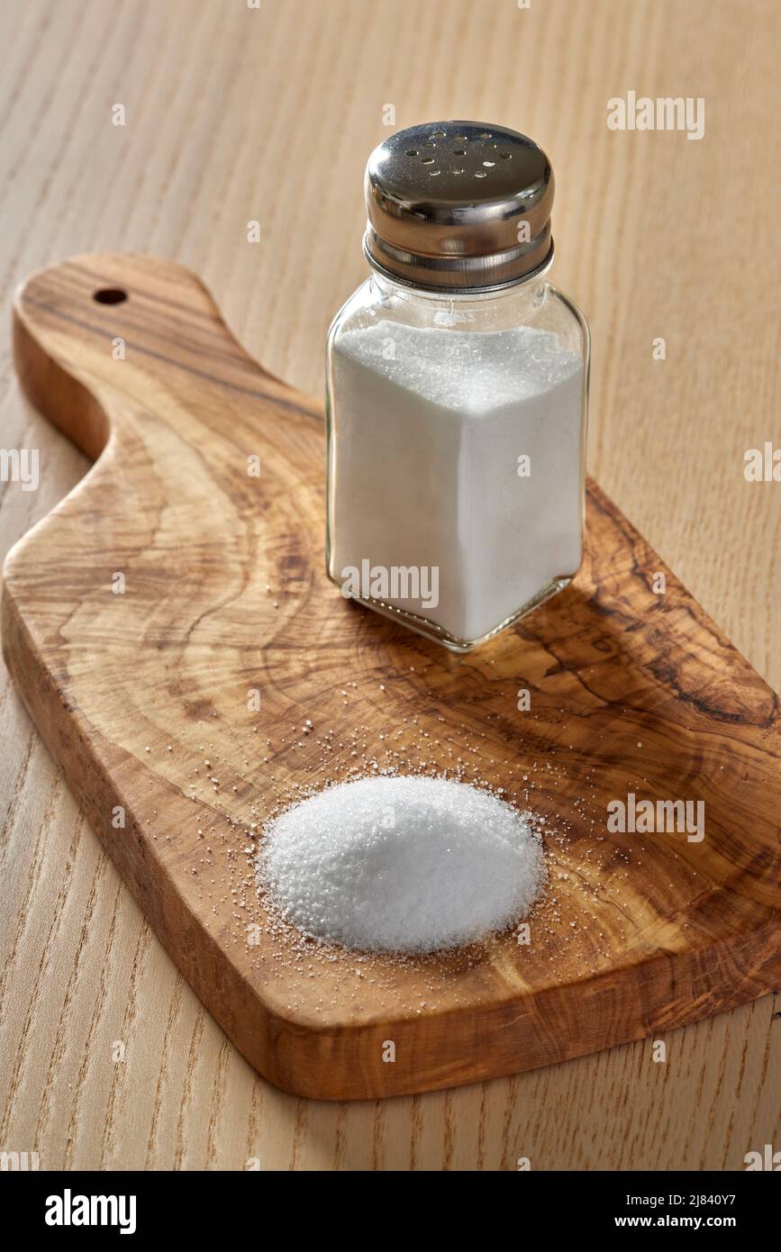 Verschüttetes Salz und ein Salzstreuer auf einem Schneidebrett aus Olivenholz Stockfoto