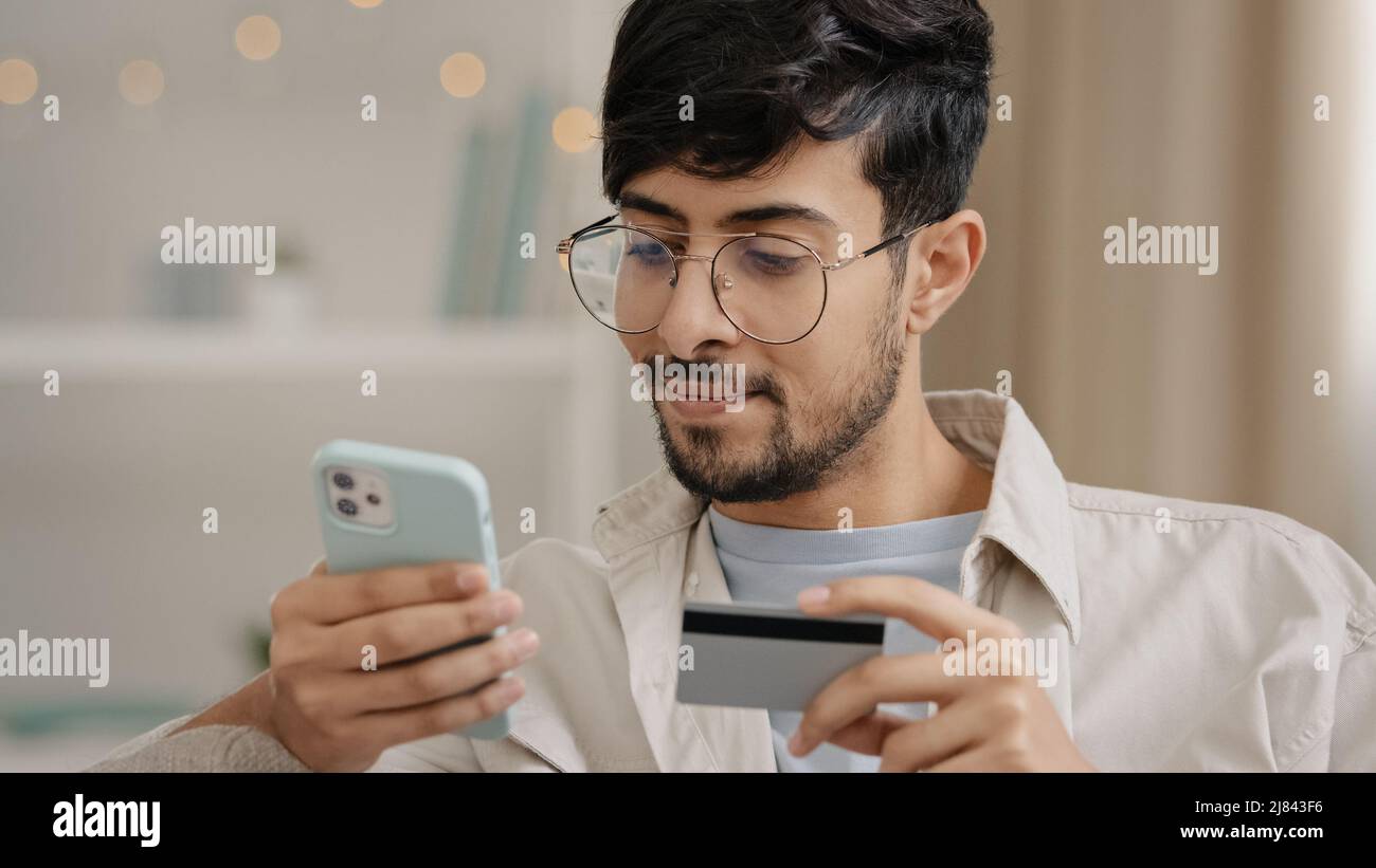 Nahaufnahme bärtiger arabischer Geschäftsmann in Brille mit Kreditkarte und Telefon macht Kauf Online-Shopping gibt Banknummer Online-Transaktion verwendet Stockfoto