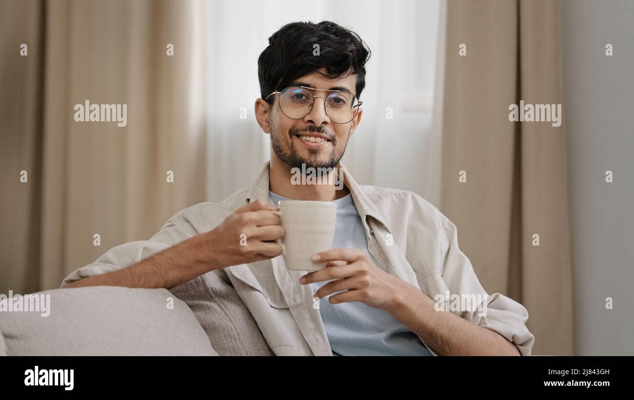 Arabisch bärtig Millennial Mann latein Mann in Gläsern sitzen zu Hause genießen köstliche heiße Früchte Kräutertee Kaffee trinken Kakao trinken Cappuccino Stockfoto
