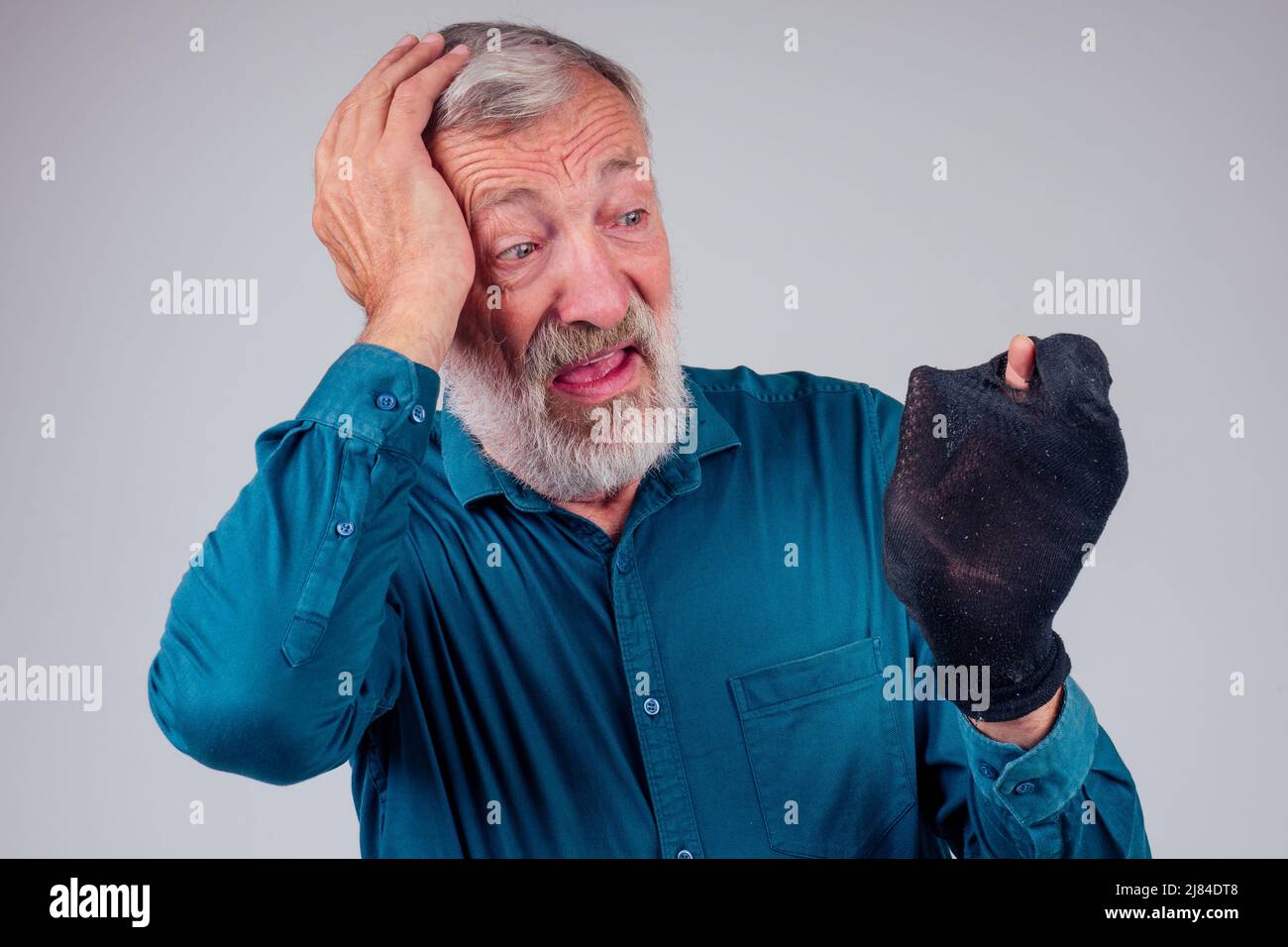 Kopf- und Schulterportrait eines älteren Mannes, der sein Gesicht aufgeschrumpft hat, während er seine Nase hält und stinkende Socken auf weißem Hintergrund hält Stockfoto