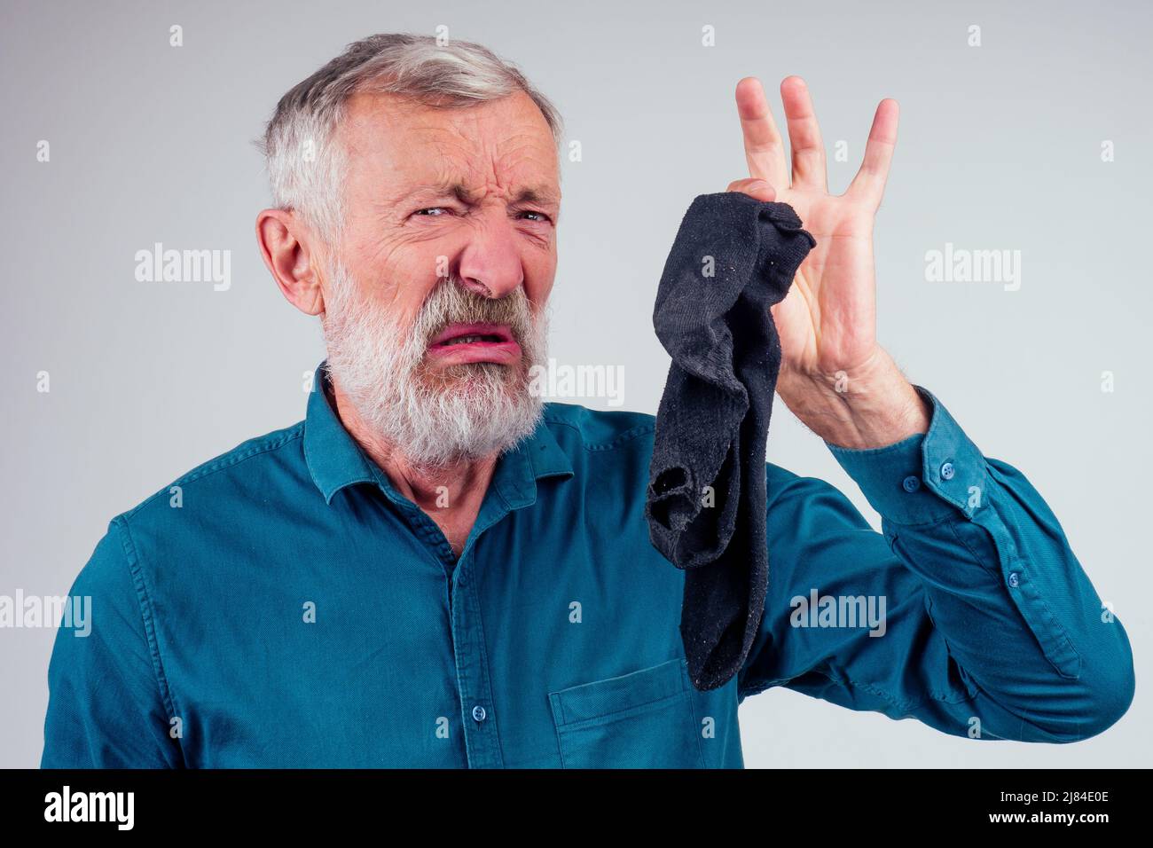 Kopf- und Schulterportrait eines älteren Mannes, der sein Gesicht aufgeschrumpft hat, während er seine Nase hält und stinkende Socken auf weißem Hintergrund hält Stockfoto