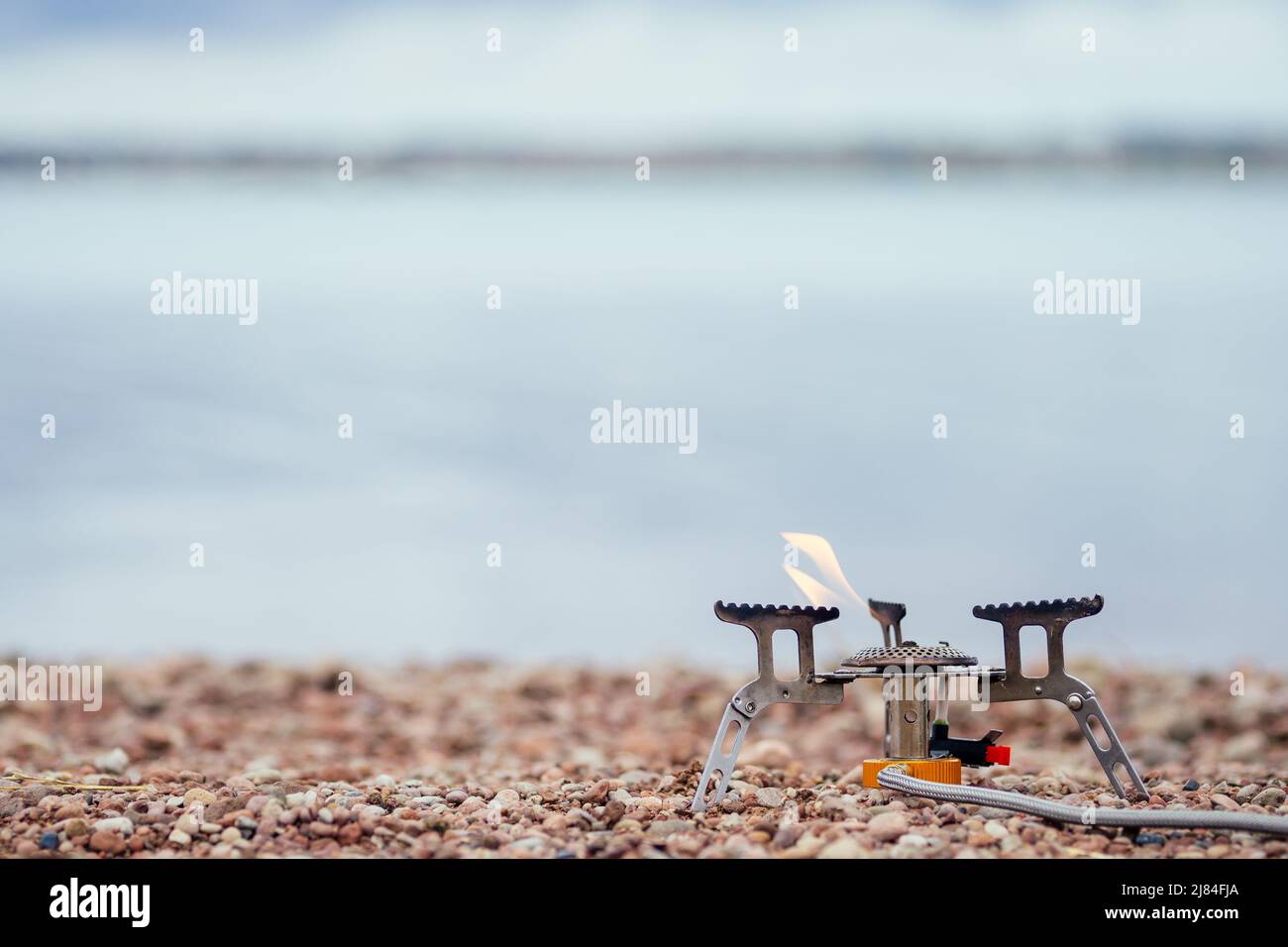 Die Pfanne mit dem Brei steht auf dem Gasbrenner (Campingkocher). Auf dem Hintergrund des Flusses Stockfoto