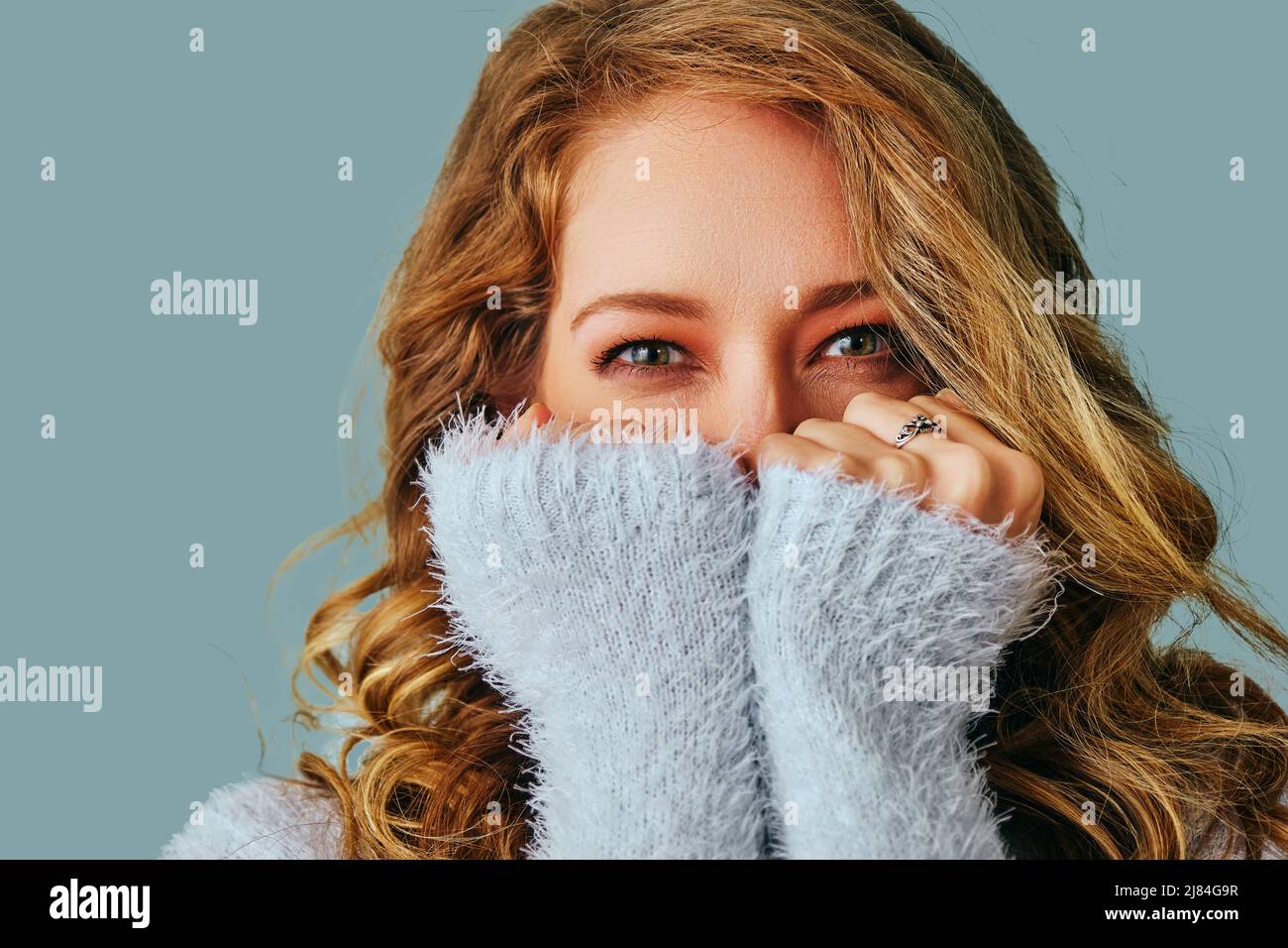 Porträt einer jungen lächelnden Frau mit langen Haaren bedeckt Gesicht mit Händen Studio Stockfoto