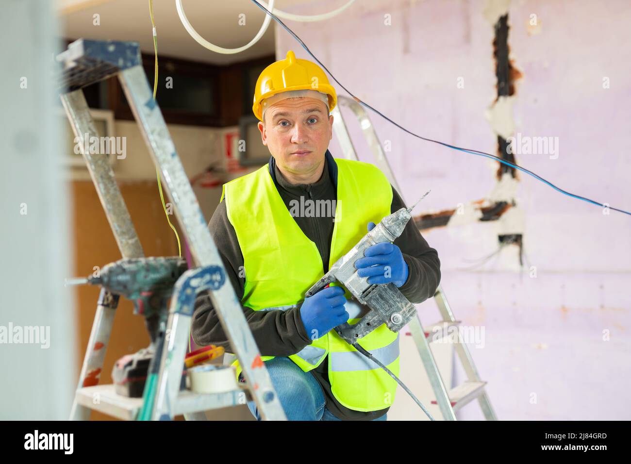 Ein männlicher Unternehmer hat sich mit einer Schraubpistole bei Überholungen in Innenräumen an der Trockenbaumontage beteiligt Stockfoto