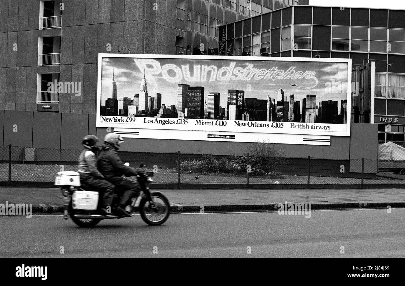 Ein Paar auf einem Motorrad passiert eine Werbetafel für British Airways auf einer Straße in London, England um 1980s Stockfoto