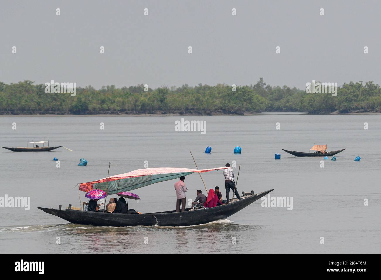 Menschen sahen, wie sie den Kholpatua-Fluss mit einem Boot in der Nähe des Sundarban-Waldes bei Shyamnagar im Satkhira-Bezirk überquerten. Tausende von Männern und Frauen gehen jeden Tag in den Sundarbans-Wald im Süden von Bangladesch, um Honig zu sammeln, Brennholz zu sammeln oder Fische, Krebse zu fangen und sich selbst einem großen Risiko für einen Tiger-Angriff zu aussetzen. Bangladesch ist eines der Länder, die am stärksten von den Auswirkungen des Klimawandels betroffen sind. Die regelmäßigen und schweren Naturgefahren, unter denen Bangladesch bereits unter tropischen Wirbelstürmen, Flusserosion, Überschwemmungen, Erdrutschen und Dürren leidet, werden sich in der Intensität und Häufigkeit als erhöhen Stockfoto
