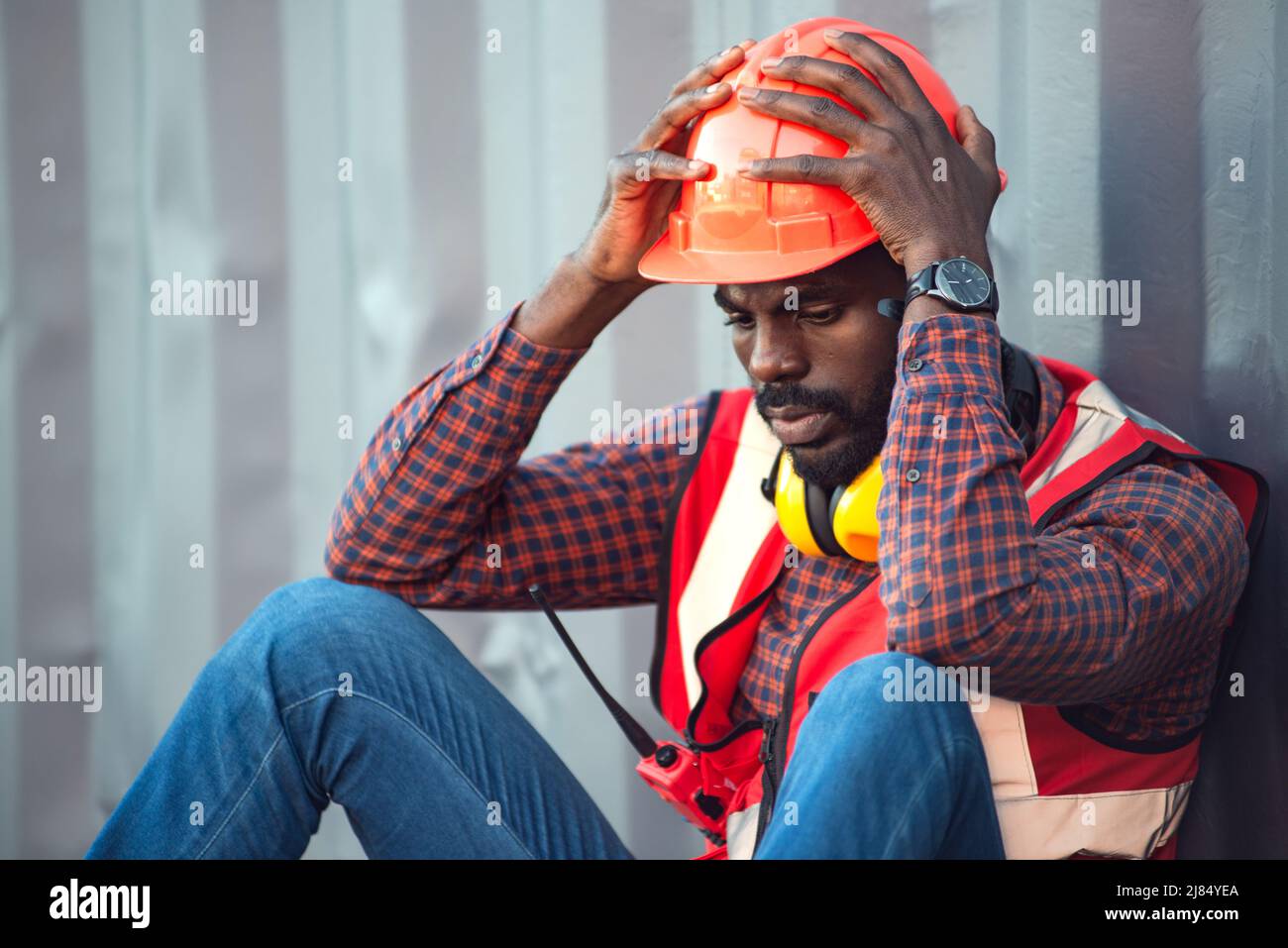 Afroamerikanischer Techniker oder Ingenieur. Setzen Sie sich in die Nähe eines Behälters und sehen Sie müde und müde oder arbeitslos aus. Logistik Industrie Cargo Mover Konzept. Stockfoto