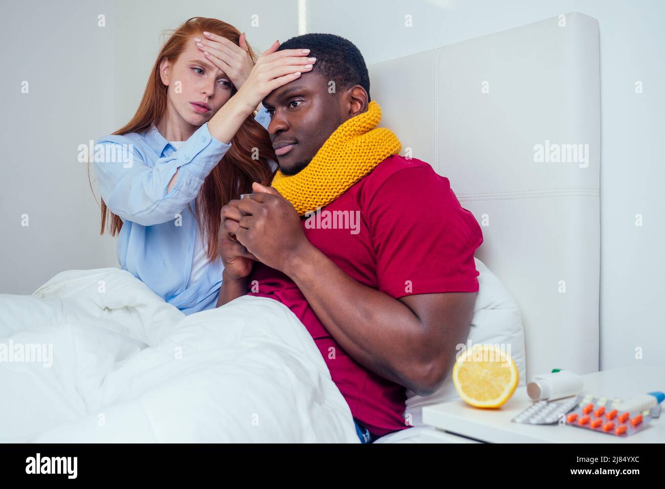 afroamerikanischer Mann im Strickschal und rothaarige Ingwer-Frau im Schlafanzug liegen im Bett Tag frei von der Arbeit, weil sie schlechte Laune sind Stockfoto