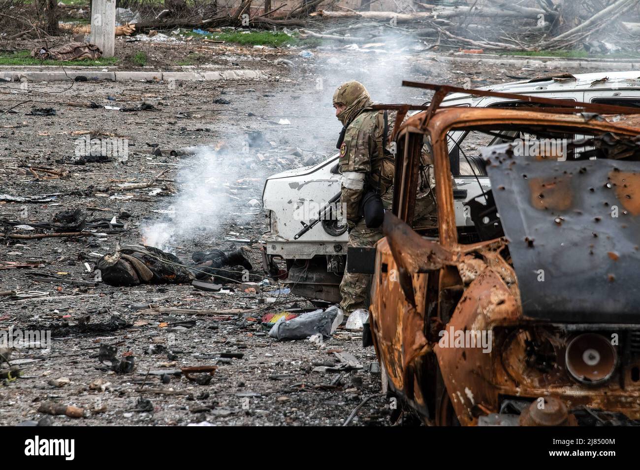 Mariupol, Ukraine. 18. April 2022. (ANMERKUNG DER REDAKTION: Bild zeigt den Tod) ein russischer Soldat steht zwischen zerstörten Autos in der Asovstalska-Straße in Mariupol, während der Leichnam eines Panzerbesatzungsmitglieds hinter ihm brennt. Der Kampf zwischen den russisch-prorussischen Streitkräften und den vom Asow-Bataillon angeführten trotzenden ukrainischen Streitkräften dauert in der Hafenstadt Mariupol an. (Bild: © Maximilian Clarke/SOPA Images via ZUMA Press Wire) Stockfoto