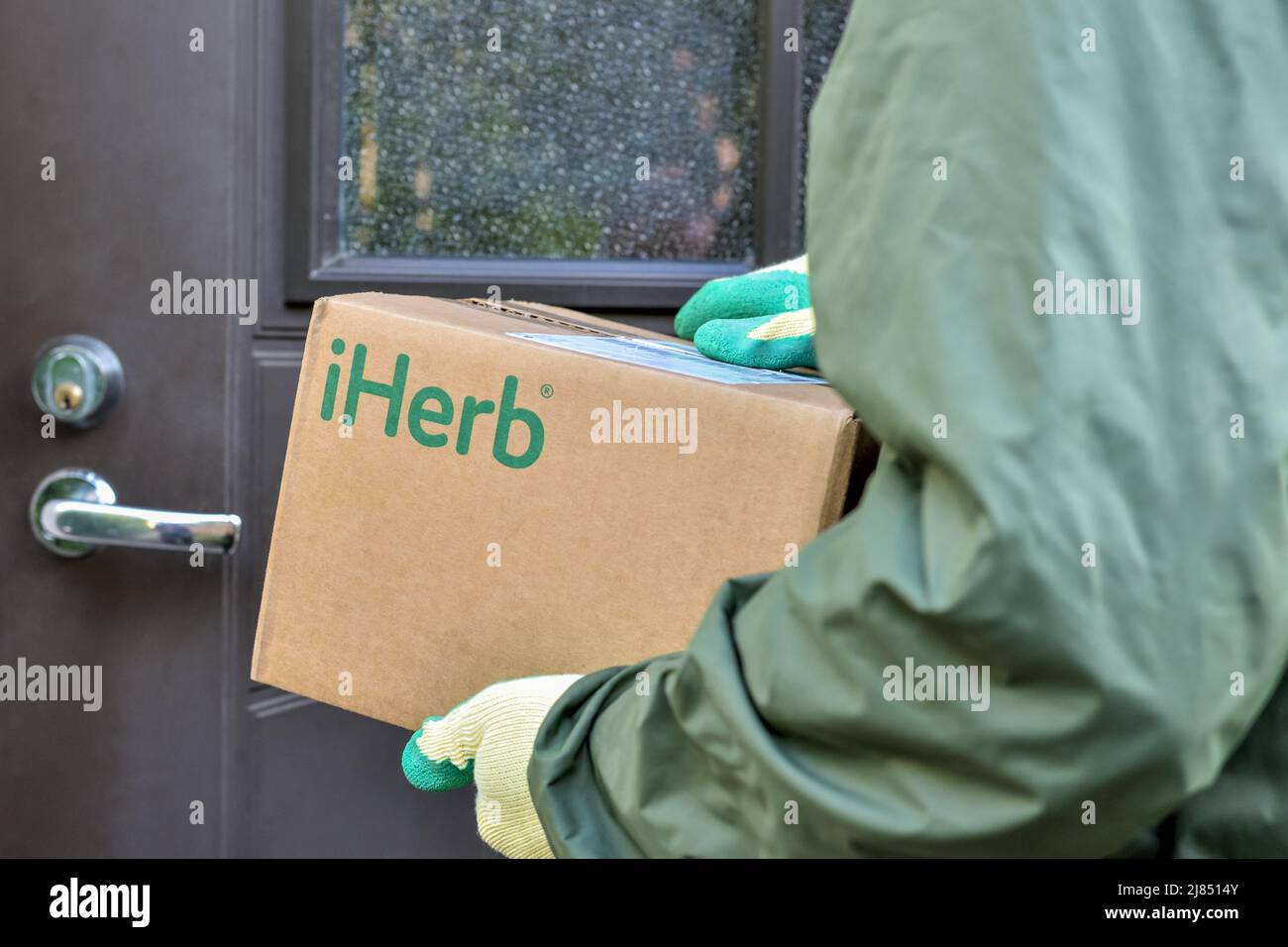 IHerb-Logo auf einem Karton in den Händen des Kuriers während der Lieferung an die Tür des Hauses: Riga, Lettland - 10. September 2021 Stockfoto