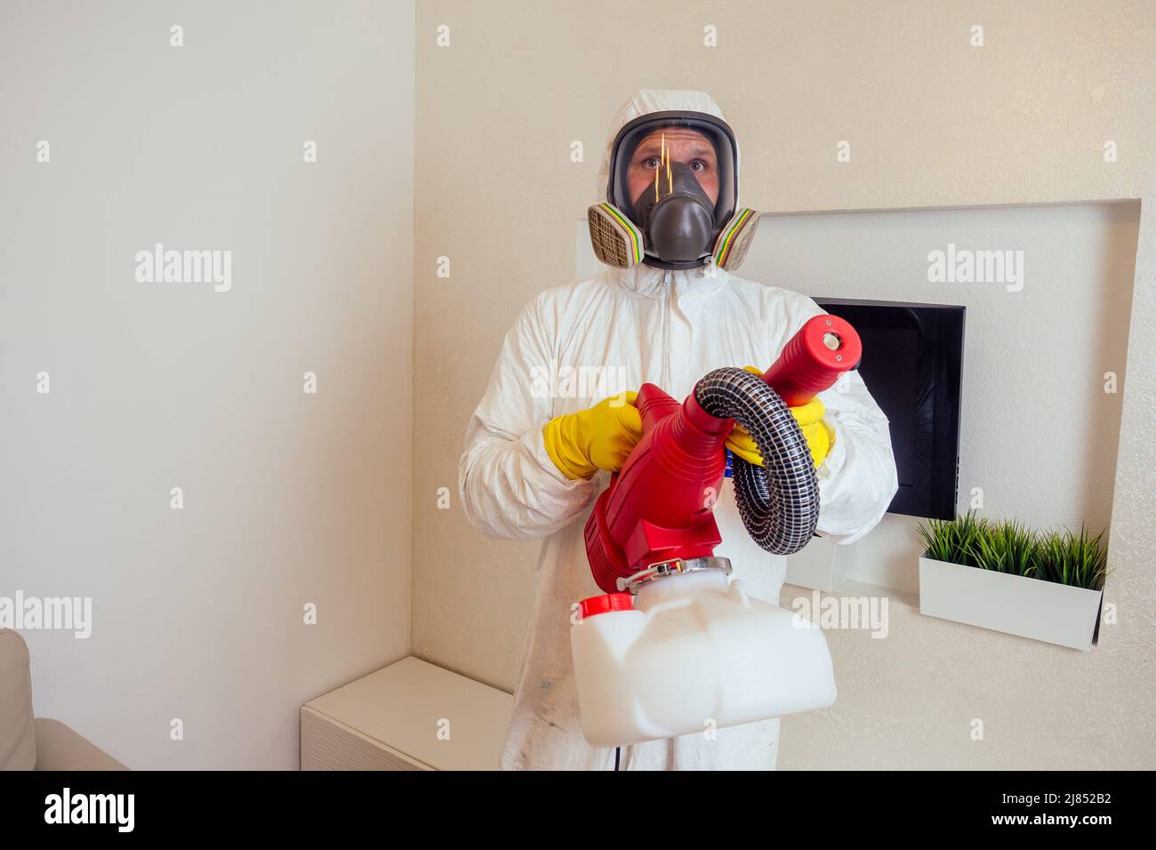 Schädlingsbekämpfer in Uniform sprühen Pestizide unter der Couch im Wohnzimmer Stockfoto