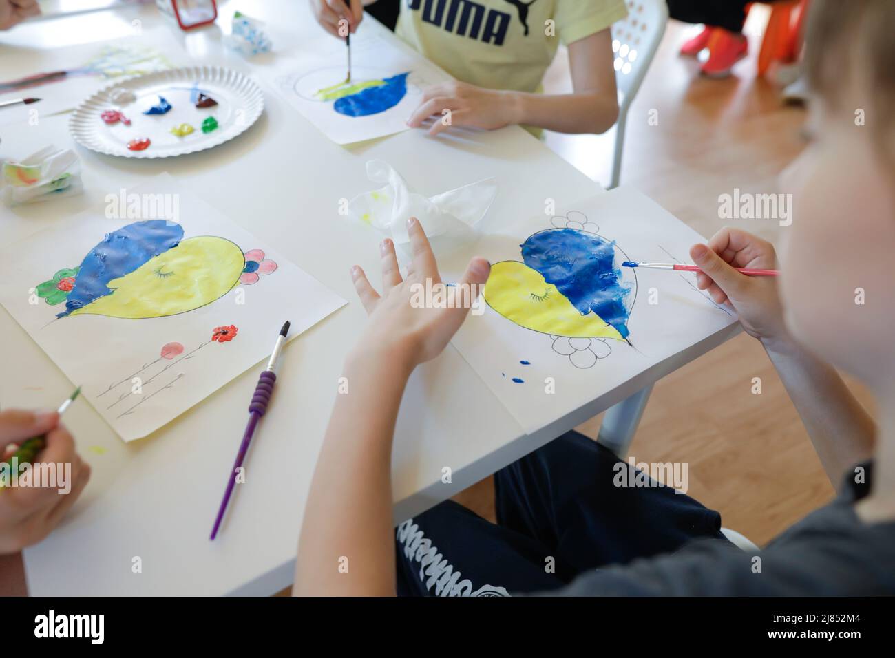 Bukarest, Rumänien - 9. Mai 2022: Details zur geringen Schärfentiefe (selektiver Fokus) mit ukrainischen Flüchtlingskindern, die eine herzförmige ukrainische Flagge zeichnen Stockfoto