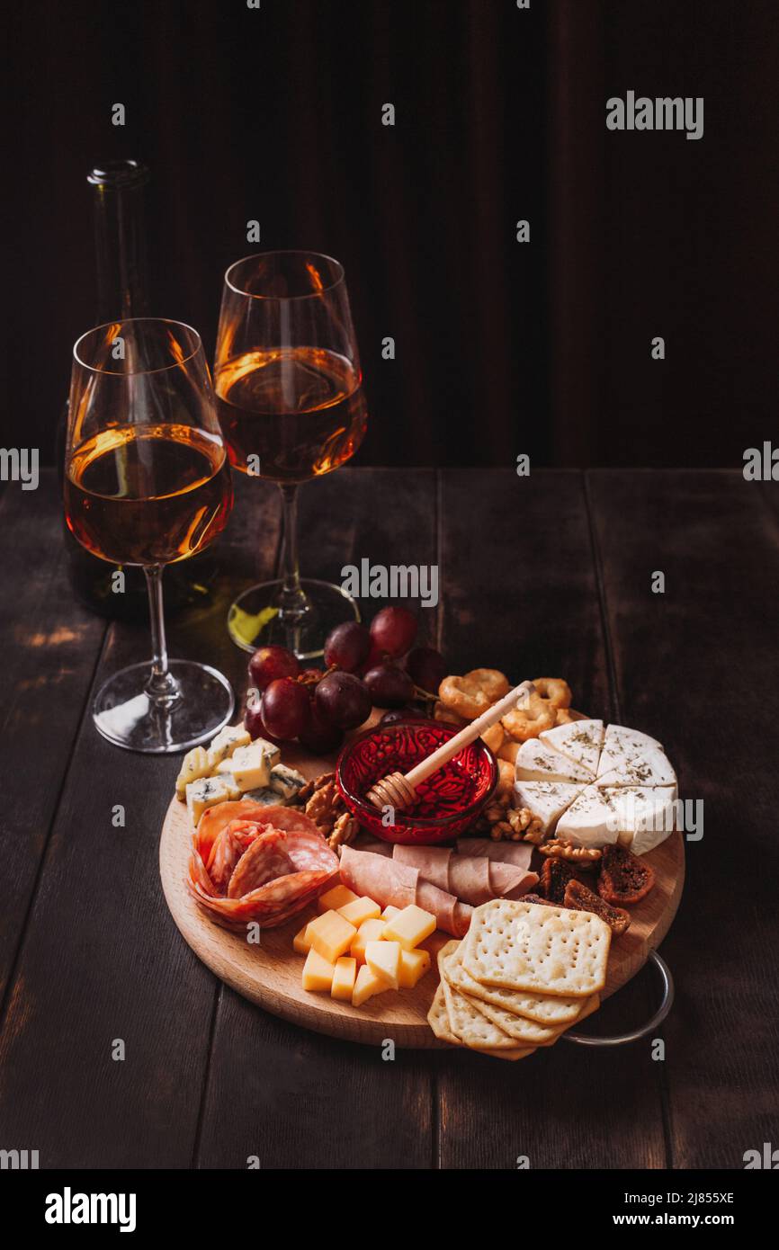 Wurst und Käse, geschnitten mit Obst, Keksen und Sauce, mit zwei Gläsern weißem Portwein und einer Flasche. Aufschnitt und Käseplatte Stockfoto