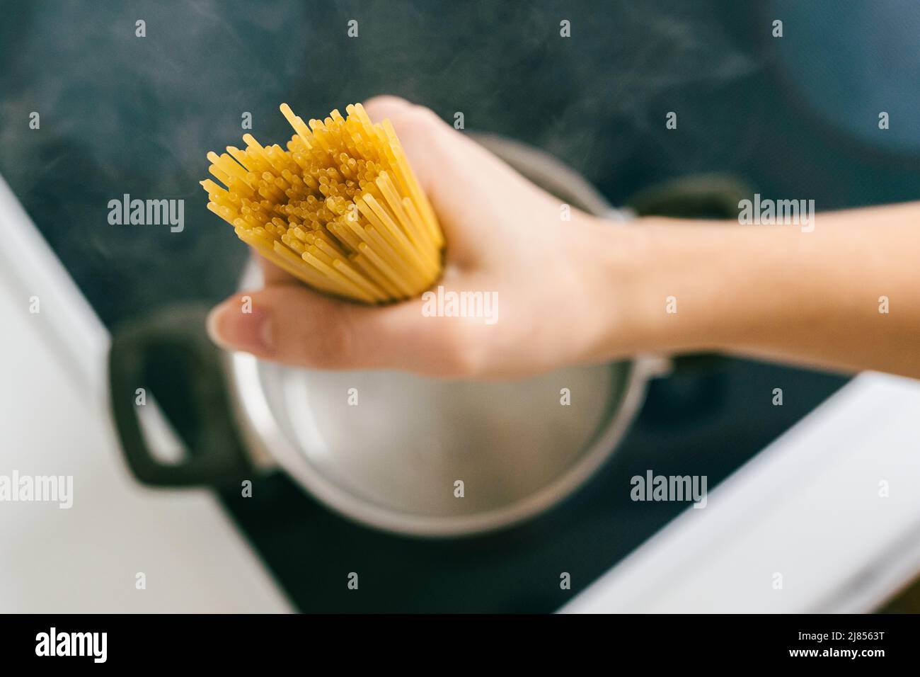 Hand legt Spaghetti in Topf mit kochendem Wasser. Kochen Pasta, Zutat für Bolognese Rezept. Glutenfreie Pasta, gesunde Lebensmittel Stockfoto