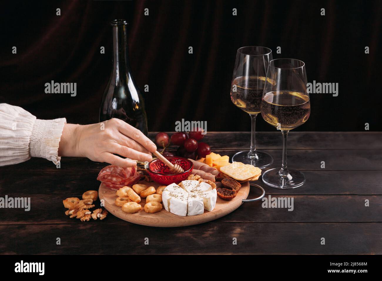 Die Hand der Frau nimmt ein Stück Käse aus dem Vorspeisen-Brett mit verschiedenen Käsesorten, Fleisch, Wurstrosette, Trauben und Keksen. Stockfoto