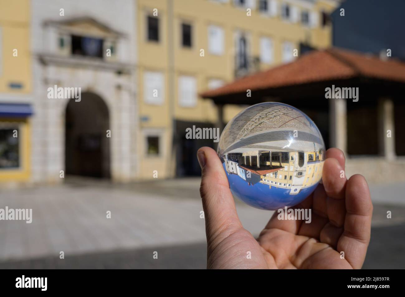 Hand hält Glaskugel vor dem alten Stadttor und Marktplatz in Cres (Kroatien) Stockfoto
