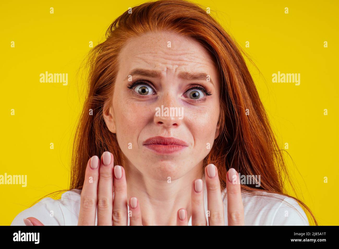 Nahaufnahme Porträt einer nervösen unglücklichen jungen rothaarigen Ingwerfrau, die auf einen gebrochenen Fingernagel schaut und weint. Nackte Maniküre auf gelbem Hintergrund im Studio Stockfoto