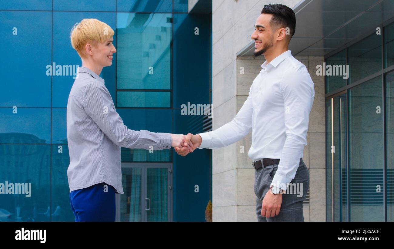 Zwei multiethnische Kollegen arabischen Mann und kaukasische Frau Geschäftspartner stehen im Freien in der Nähe von Firmengebäude reden schütteln Hände schließen Deal Stockfoto