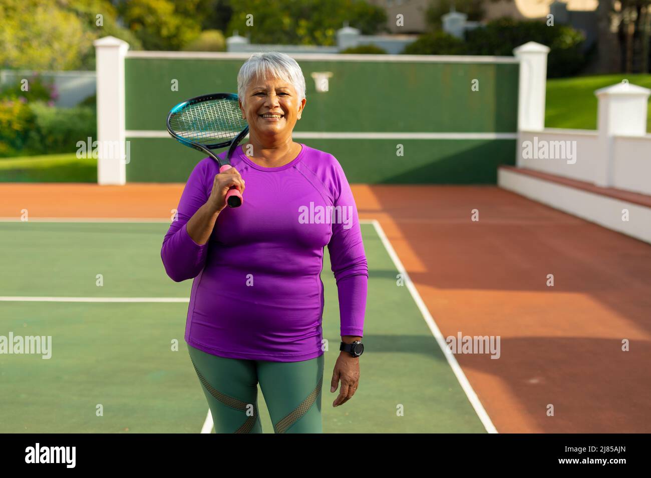 Porträt einer selbstbewussten, lächelnden älteren Frau aus der Birazialzeit mit kurzen Haaren und Tennisschläger auf dem Tennisplatz Stockfoto