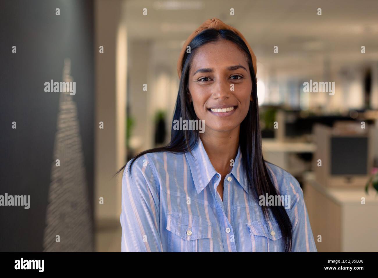 Porträt einer lächelnden, schönen, afroamerikanischen Geschäftsfrau mit langen schwarzen Haaren am Arbeitsplatz Stockfoto