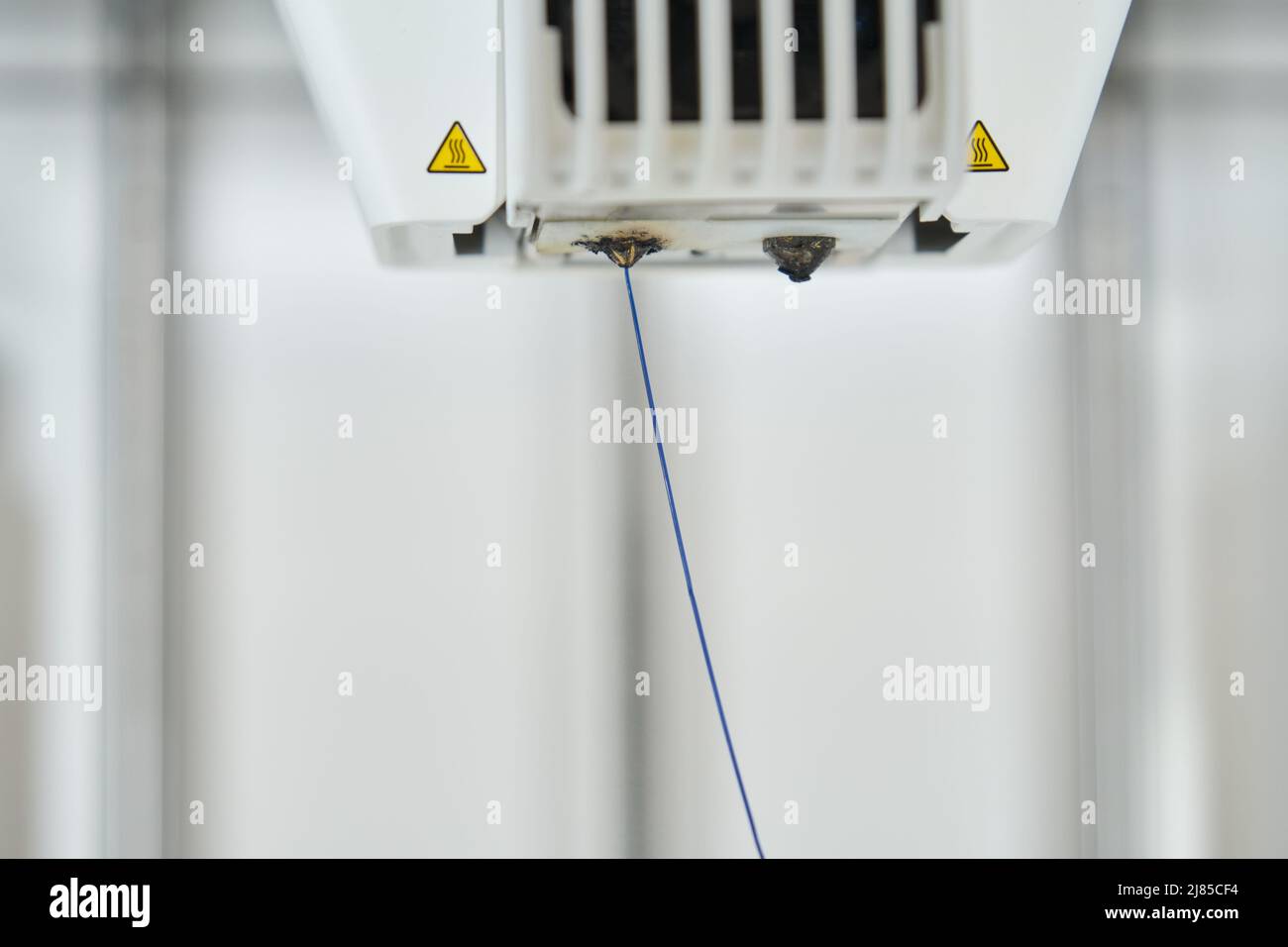 Blaues Kunststofffilament, das durch die Düse des Druckers 3D extrudiert. Stockfoto