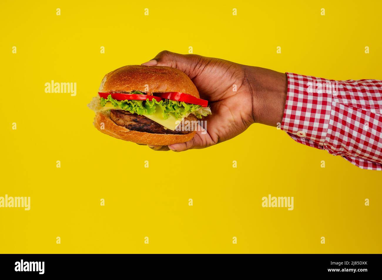 Junger afroamerikanischer Mann, der Hamburger isst, isoliert auf gelbem Hintergrund, Hände aus der Nähe Stockfoto