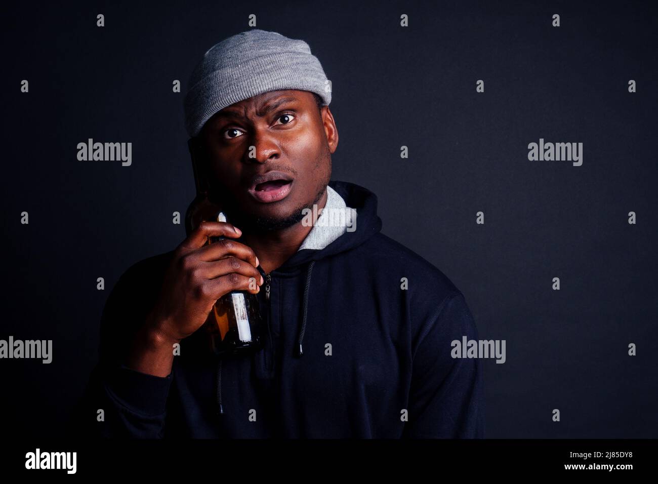 afroamerikanischer Mann hält eine Flasche Wein und fühlt sich Kopfschmerz Scheiße in Studio schwarz background.bum obdachlos ertrinken den Schmerz Stockfoto