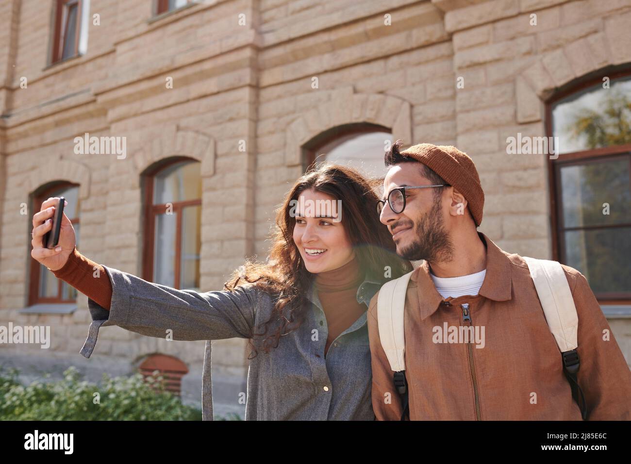 Fröhliches junges multiethnisches Paar von Touristen, die gegen Steingebäude stehen und gemeinsam Selfie machen Stockfoto