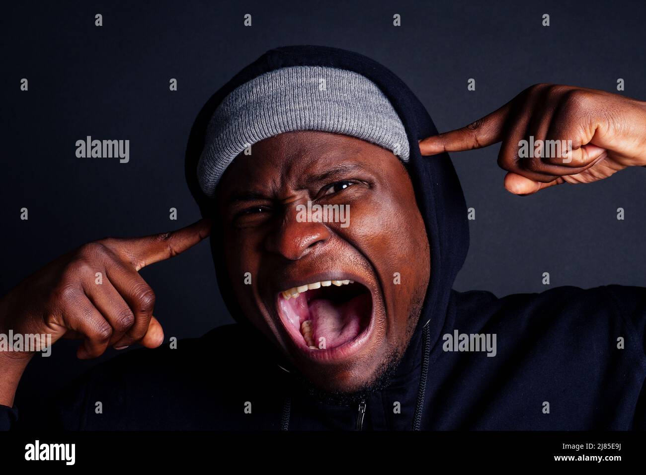 Besorgt afroamerikanischen Gesichtsmann trägt grauen Hut und schwarzen Hoodie mit Kapuze, laut schreiend und verstopfte Ohren ich will nicht hören. Opfer Stockfoto