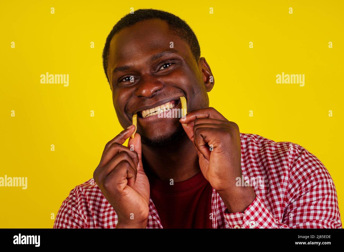 Gutaussehender lateinischer Mann, der auf gelbem Hintergrund Pommes isst, mit Appetit und Genuss Stockfoto