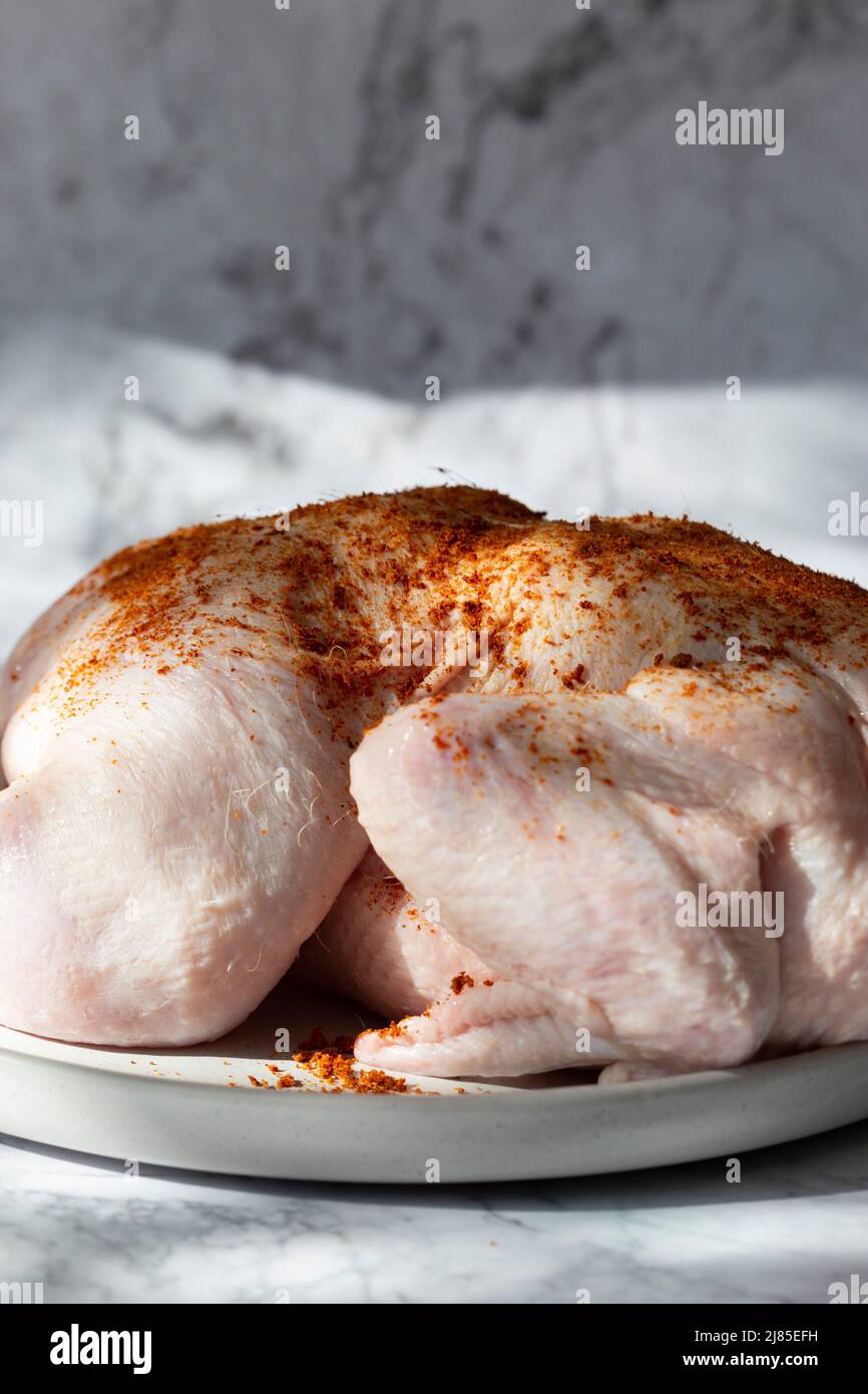 Rohes ganzes Huhn mit Paprika auf einem Teller gewürzt. Auf Marmorboden Stockfoto