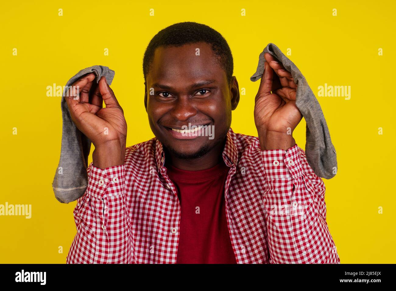 Unzufriedener afroamerikanischer Mann schließt die Nase, fühlt sich über Socken übel gerochen, trägt lässiges rotes T-Shirt auf Studio-gelbem Hintergrund Stockfoto
