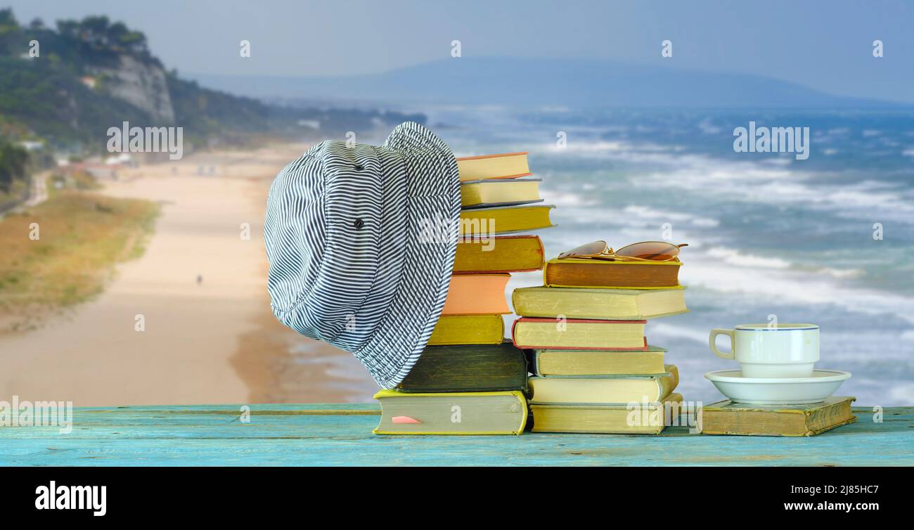 Stapel von Büchern, Hut und Sonnenbrille vor der schönen Meereslandschaft, Lesen in den Sommerferien und Entspannungskonzept Stockfoto