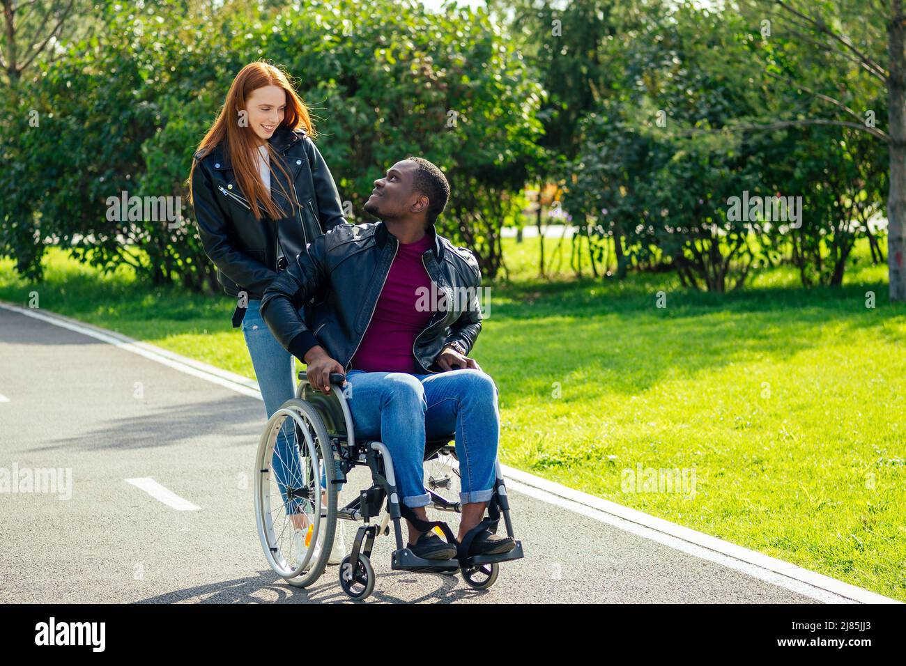 afro-amerikanischer Mann auf Rollstuhl sitzend, seine rothaarige Ingwer-Freundin Rolling Kinderwagen im Herbst Park. Mit romantischen Datum Stockfoto